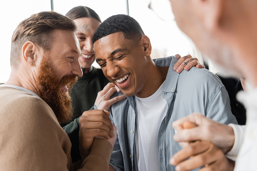 Positive people hugging african american man during alcoholics meeting and therapy in rehab center. PHP